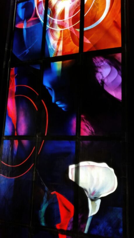 Figurative stained glass detail of the Annunciation with calla lily and abstracted figure, painterly glass composition for church setting