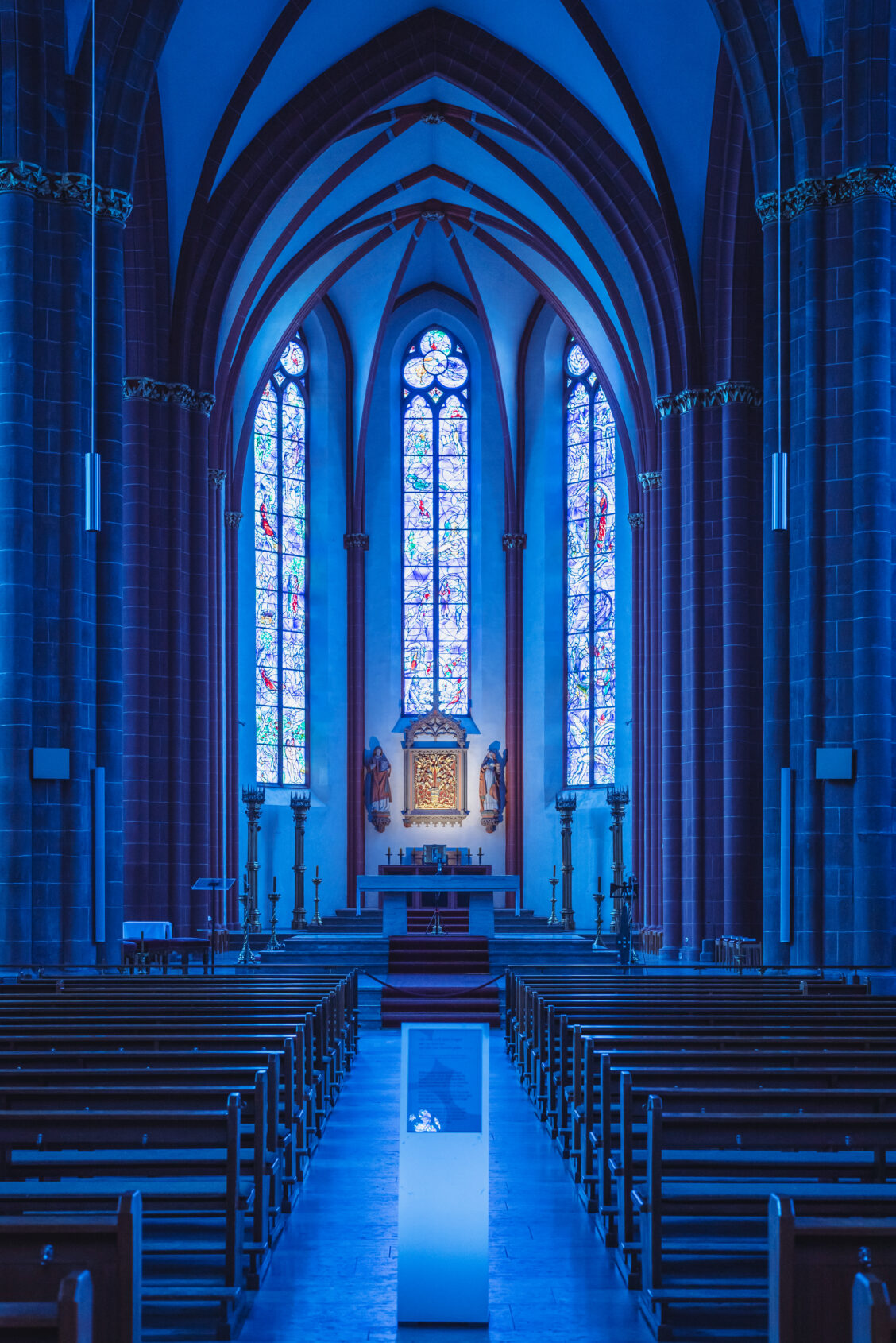 View to the main altar with blue stained glass windows in the background inside the church St. Stephan in Mainz